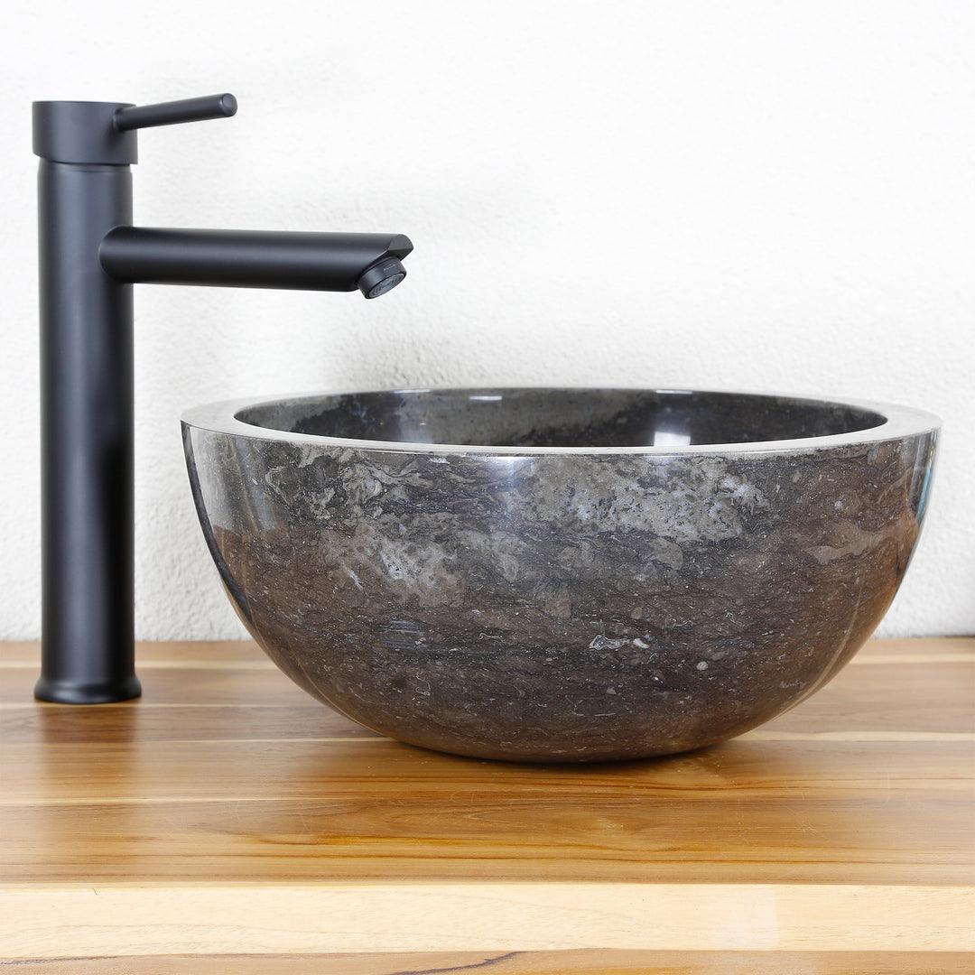 Rundes Steinwaschbecken aus dunklem Naturmaterial als Aufsatz auf Holzplatte mit schwarzer Armatur, cleanes Studio-Setting